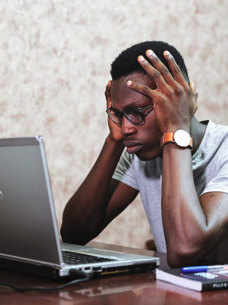 A man staring at a laptop with his head in his hands, looking frustrated